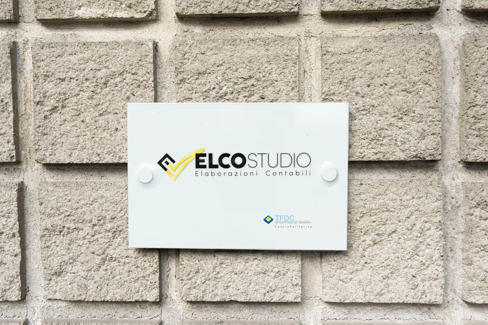 Un'insegna bianca su un muro di pietra con logo “ELCOSTUDIO” con il tagline “Elaborazioni Contabili”.