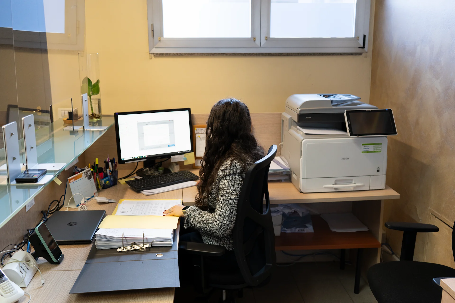 Donna seduta a una scrivania, concentrata mentre lavora al computer con documenti sparsi intorno
