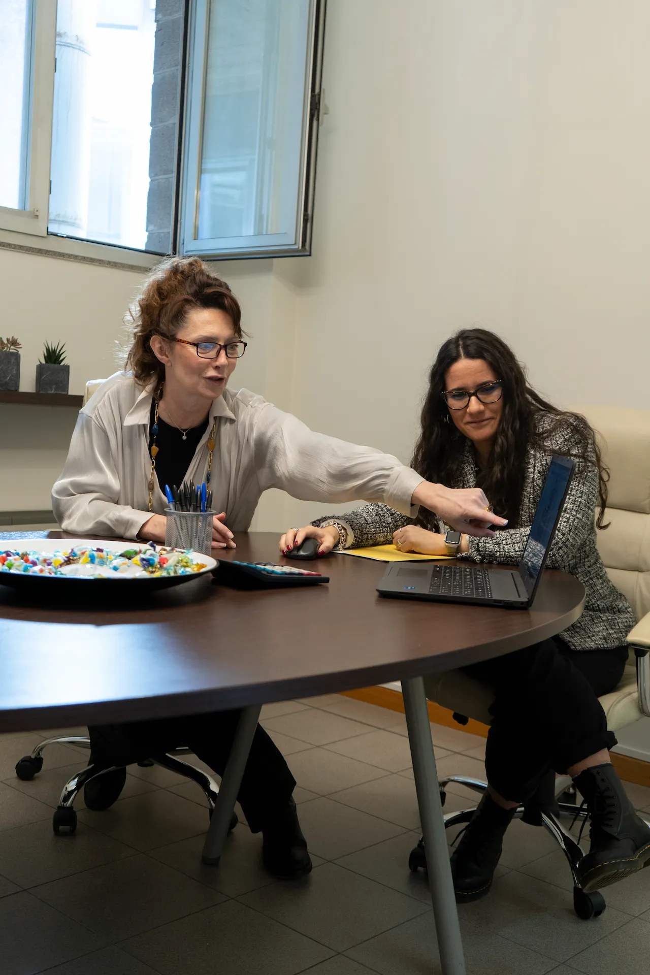 Due donne sedute a un tavolo, conversando e sorridendo, in un ambiente accogliente e luminoso